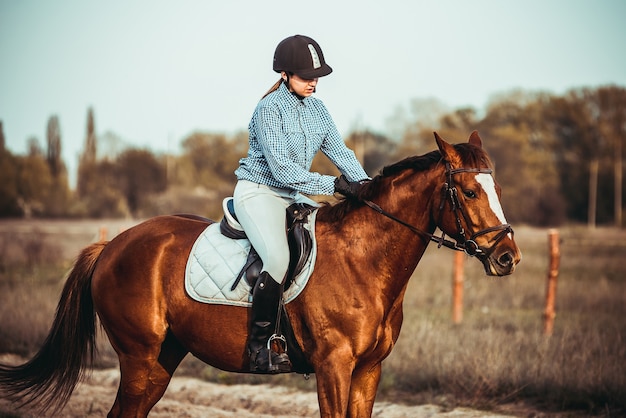 Cowgirl in een hoed die bij een paard in een veld staat