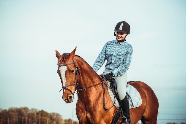 Cowgirl in een hoed die bij een paard in een veld staat