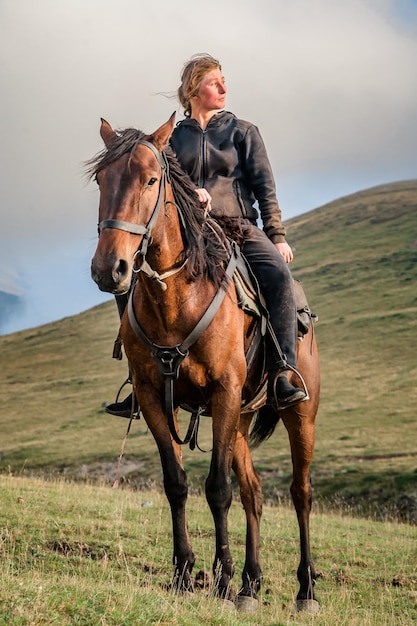 Photo a cowgirl shepherd rider on a horse gallops through a mountain valley on autumn day sky with clouds