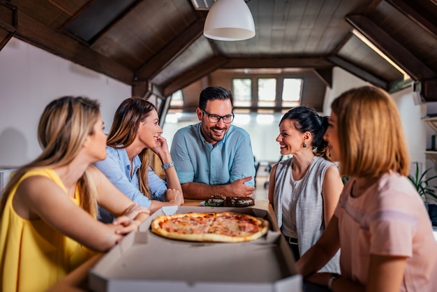 Coworkers eating pizza during work break at modern office.