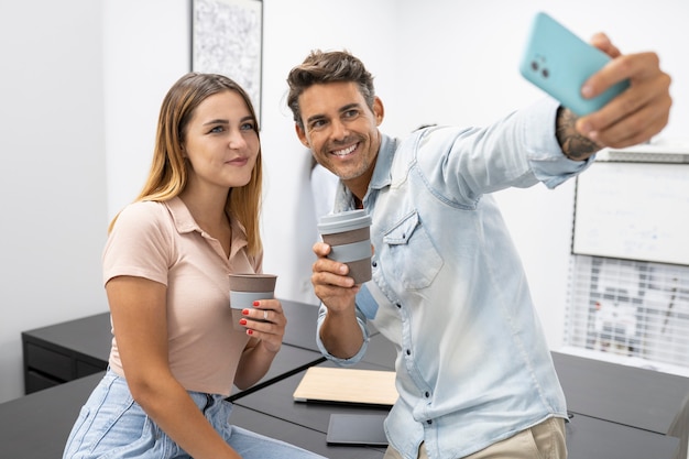 Coworkers man and woman taking selfie with smartphone and coffee