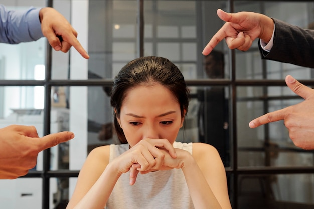 사진 동료들은 좌절한 젊은 여성 사업가를 실수로 부끄럽게 여기고 손가락으로 그녀를 가리키고 있다