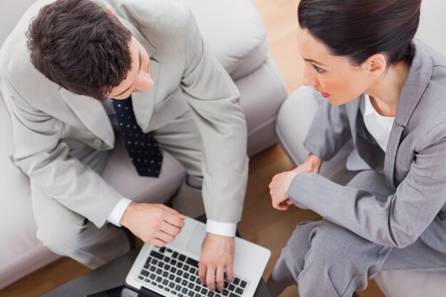 Coworkers talking and using laptop sitting on sofa 