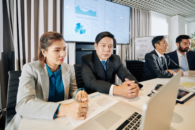 Coworkers watching presentation on laptop and discussing data in reports