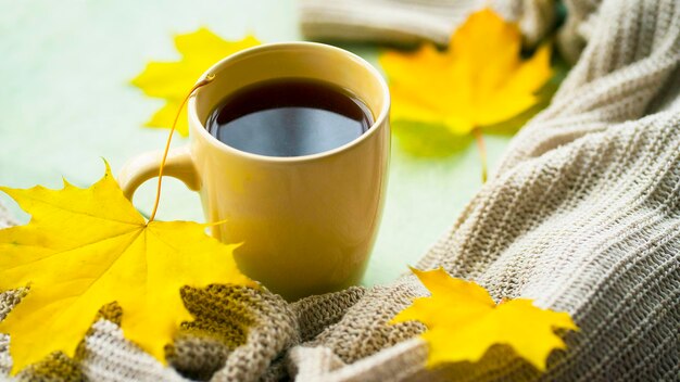 Cozy autumn composition. A cup of hot tea, a warm sweater and yellow leaves