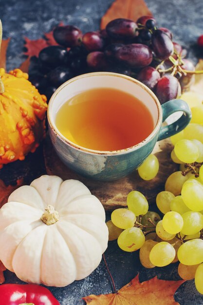 Cozy autumn composition cup of tea pumpkins grapes autumn leaves on dark stone table seasonal decoration for Halloween or Thanksgiving day