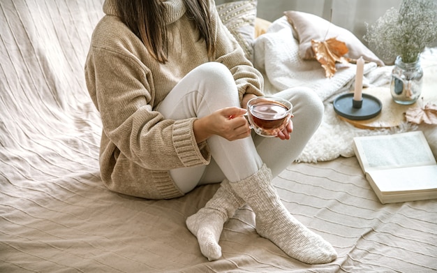 Foto accogliente autunno a casa, una donna in un maglione lavorato a maglia con una tazza di tè.