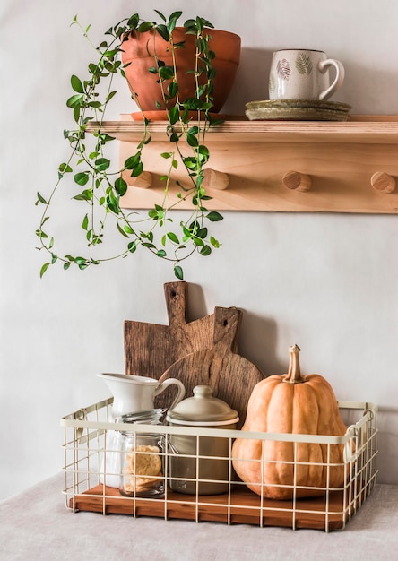 Cozy autumn kitchen interior wooden shelf with a flower dishes and a metal basket with cutting boards a pumpkin a jug on the table Cozy home interior