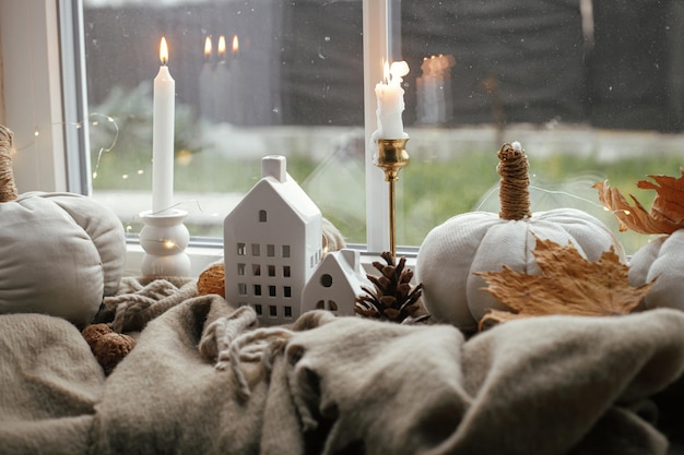 Cozy Autumn Stylish pumpkin pillows fall leaves candle lights and cute buildings decoration on brown scarf on windowsill Autumn hygge fall home decor Happy Thanksgiving