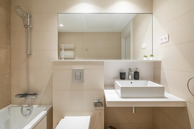 Cozy bathroom in modern design with huge mirror on the wall and bright lighting walls are in beige