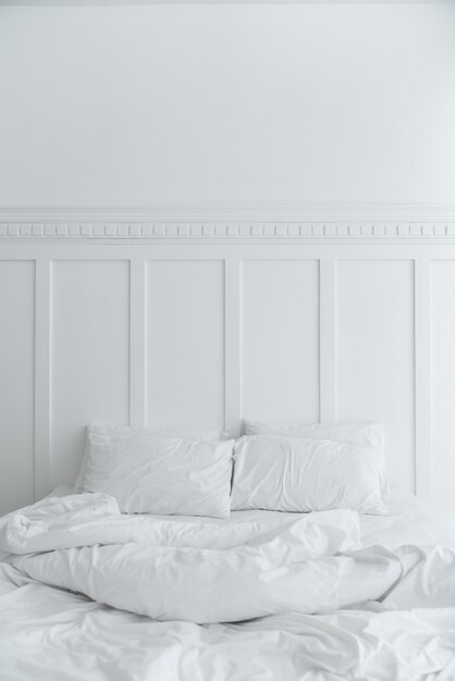 Cozy bedroom setting with two pillows and messy blanket on white painted wall