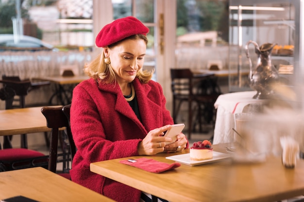 Cozy cafe. Stylish mature elegant lady wearing red coat sitting in cozy cafe drinking tasty coffee