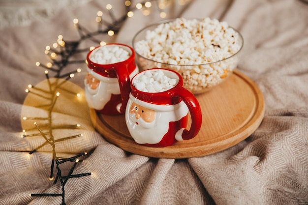 Cozy Christmas composition. Two mugs of hot drinks and marshmallows. a plate of popcorn.