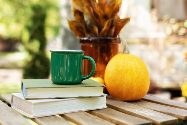 Photo cozy composition with cup of hot tea, stack books and pumpkin on table