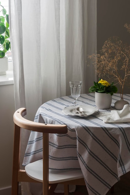 A cozy corner of the living room a table set for dinner with a tablecloth and dishes a chair