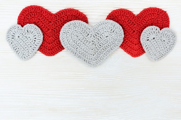 Cozy cute knitted hearts on white wooden with copy space.Top view.