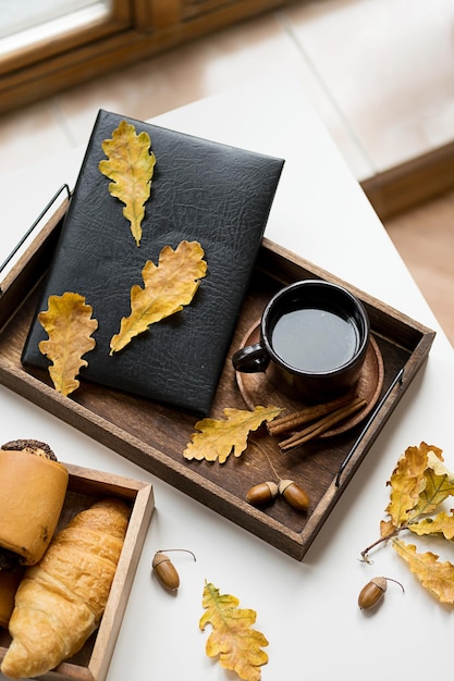 Cozy fall morning at home Coffee cup book and autumn leaves on wooden tray