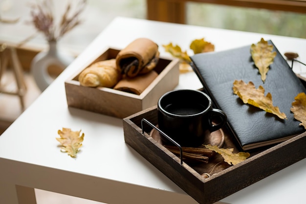 Cozy fall morning at home Coffee cup book and autumn leaves on wooden tray