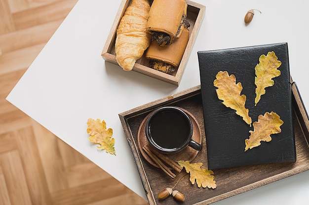 Cozy fall morning at home Coffee cup book and autumn leaves on wooden tray