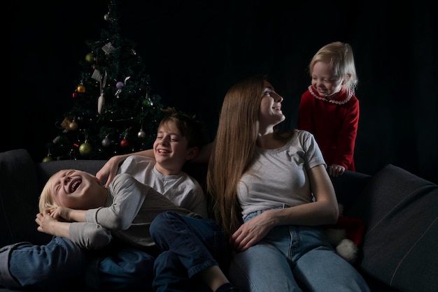 Cozy family evening - mom and three happy smiling children against the background of the Christmas tree.