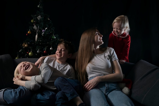 Serata in famiglia accogliente - mamma e tre bambini sorridenti felici sullo sfondo dell'albero di natale.