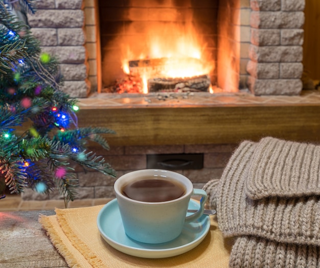 Cozy fireplace and a cup of tea on wooden table, in country house, winter vacation.