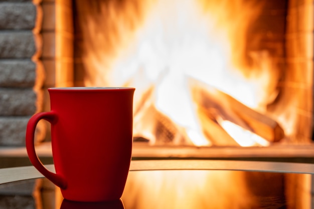 Photo cozy fireplace scene and big mug of tea, reflection from a fire on a glass table.