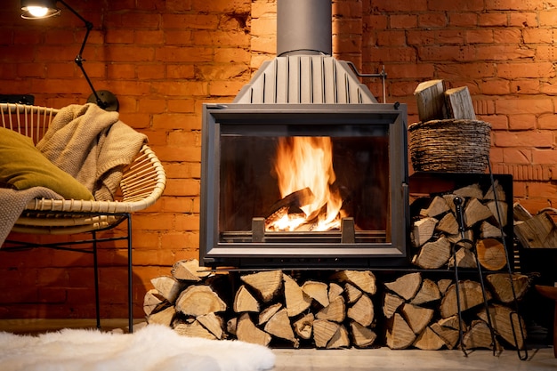 Cozy fireplace with firewood in the loft style home interior with brick wall background, burning fire in the fireplace, house coziness in winter