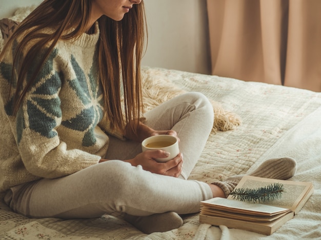 居心地の良い家。美しい女性はベッドで本を読んでいます。お茶と本でおはようございます。かなり若い女性がリラックスできます。読書のコンセプト