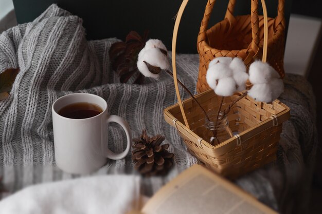 Cozy home decor with a warm atmosphere. White mug with hot tea and knitted clothes