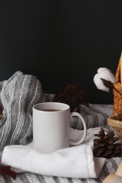 Cozy home decor with a warm atmosphere. White mug with hot tea and knitted clothes