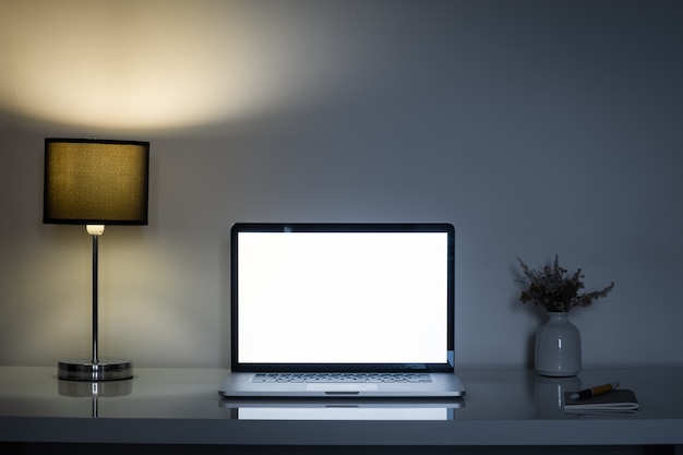 Cozy home office desk at night lit by a lamp and white laptop screen.