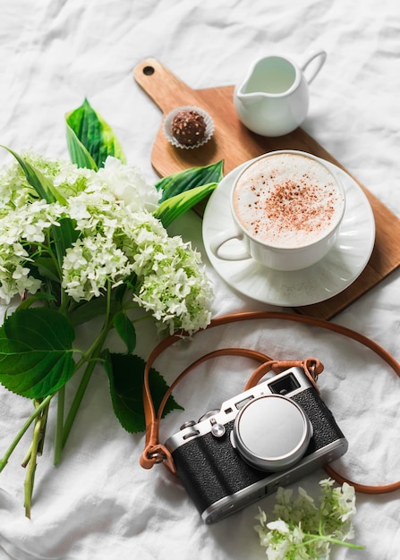 Cozy home still life cappuccino in bed bouquet of flowers and retro camera on a light background top view