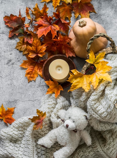 Cozy home still life knitted blanket in a straw basket pumpkin bouquet of maple leaves candle on a gray background top view