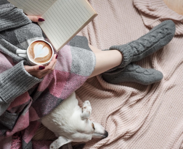 Cozy home woman covered with warm blanket drinks coffee sleeping dog next to woman