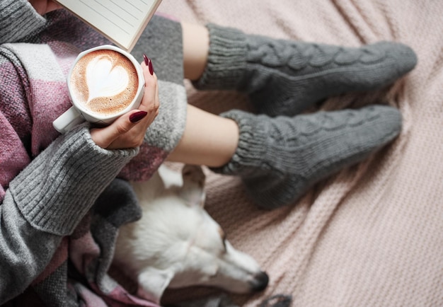 Cozy home woman covered with warm blanket drinks coffee sleeping dog next to woman