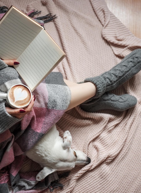 Cozy home woman covered with warm blanket drinks coffee\
sleeping dog next to woman