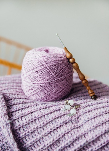 居心地の良い家庭的な雰囲気女性の趣味は暖かい色調の毛糸を編むことです紫色の女性のセーターを編むプロセスの始まり糸のボールとフック