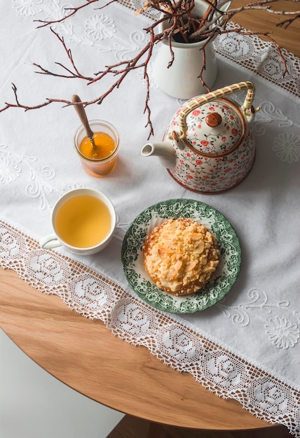 Cozy homemade morning crumble almond petals bun honey green tea on a round wooden table top view