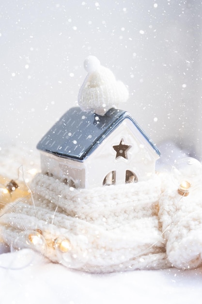 Cozy house is wrapped in a hat and scarf in a snowstorm window\
sill decor winter snow home insulation protection from cold and bad\
weather room heating system festive mood christmas new year