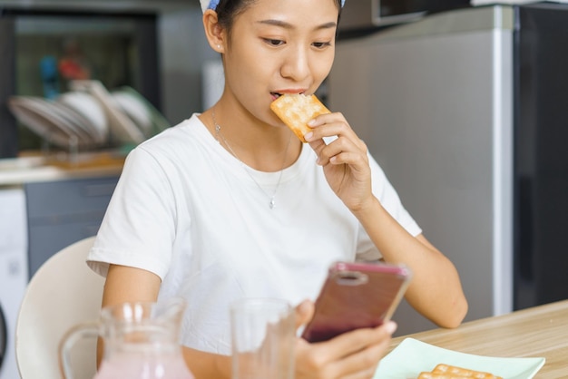 사진 아늑한 생활 방식 개념 샤워 후 터번을 입은 젊은 여성이 크래커를 먹고 소셜 미디어를 서핑합니다.