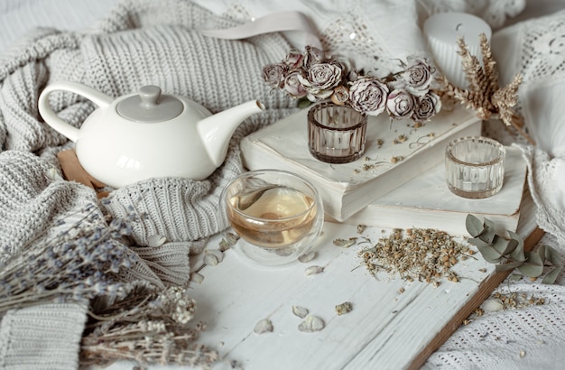 Photo a cozy light still life with candles, a cup of tea, a teapot and flowers as decor.