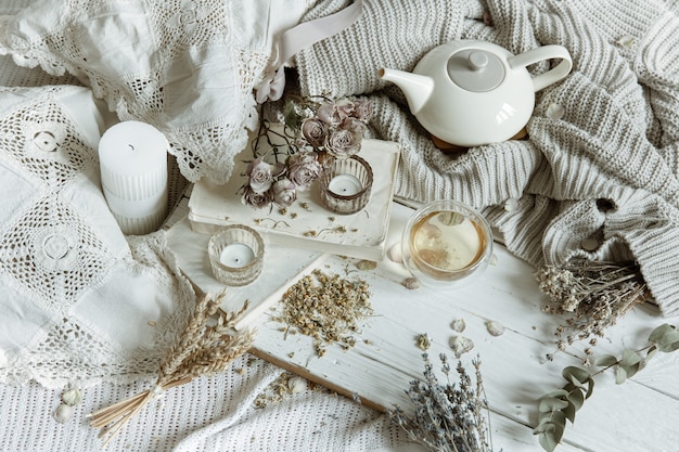 Cozy light still life with candles, tea, teapot and flowers as decor.