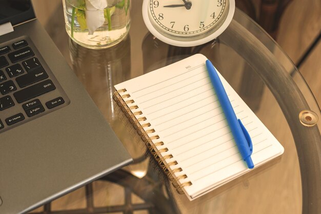 ガラスのテーブルにノートブックとラップトップを備えた居心地の良い朝のワークスペースのコンセプト
