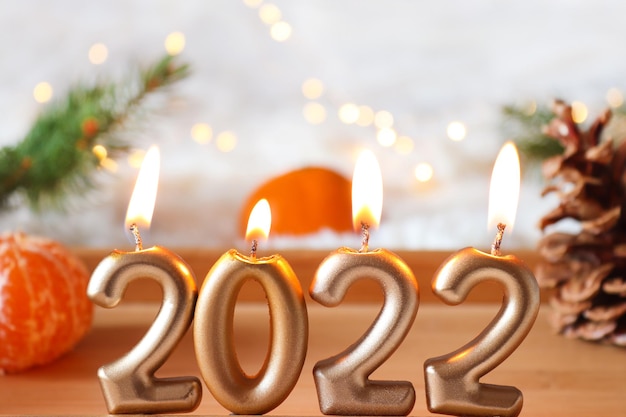 Cozy New Year composition with candlesnumbers 2022 tangerines and pine cone on wooden tray