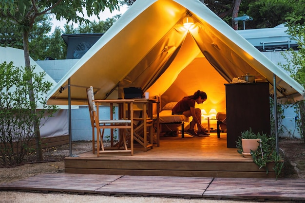 夏休みの夕暮れの豪華なキャンプ テントの中に女性と居心地の良いオープン グランピング テント