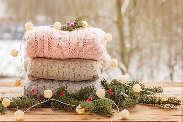 Cozy pile of knitted sweaters on wooden table on winter nature.