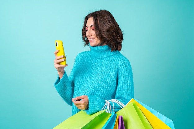 Accogliente ritratto di una giovane donna con un maglione blu lavorato a maglia e un trucco rosa brillante con borse della spesa e un telefono cellulare