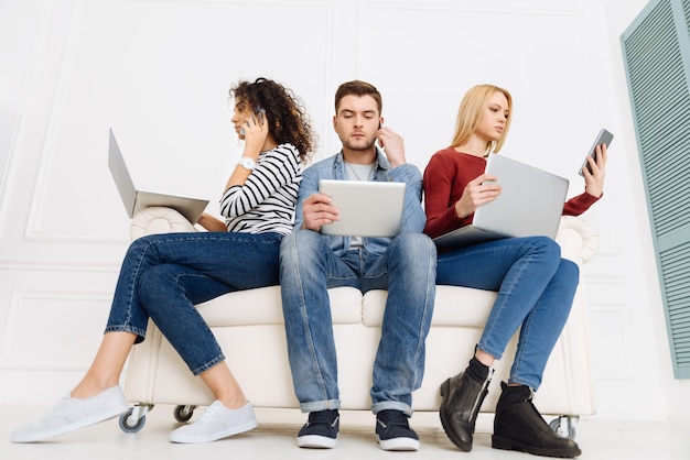 Cozy sofa. Confident girls using their gadgets and being attentive while sitting near their partner