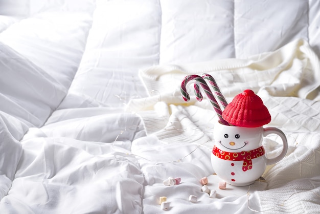 Cozy soft blanket with a cup in the form of a snowman with Christmas candies on the bed 